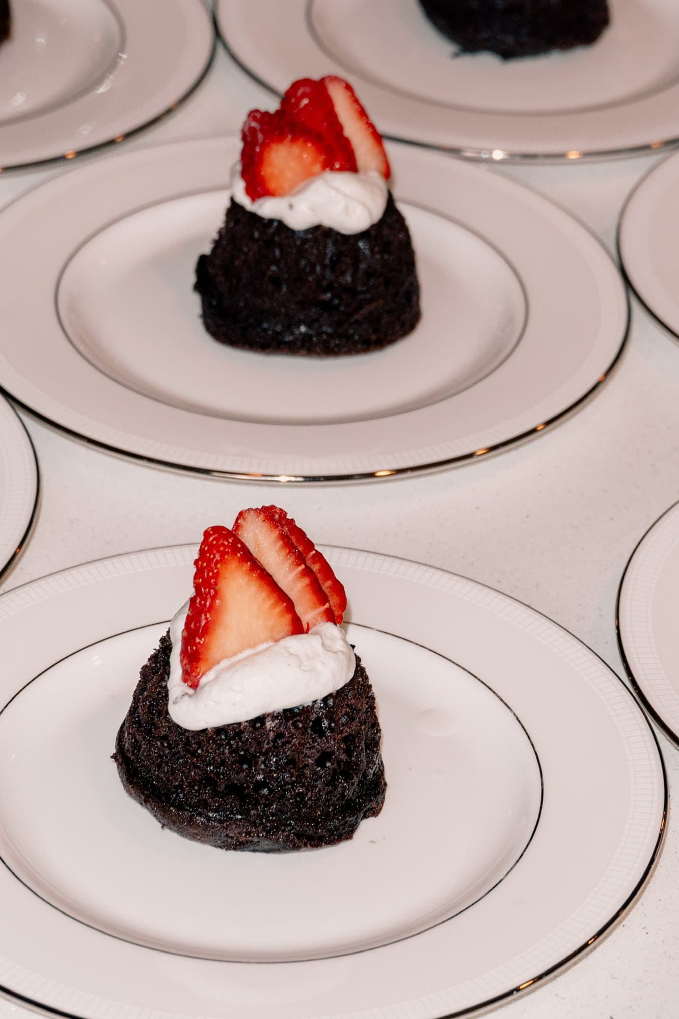 Chocolate cakes topped with cream and strawberries on gold-rimmed plates
