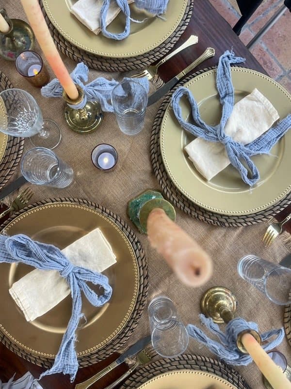 Overhead view of a dinner table with gold chargers, blue ribbon-tied napkins and taper candles